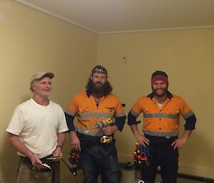 Jeff the painter and Adam and AJ both electricians standing in a partially renovated room with their tool belts on.