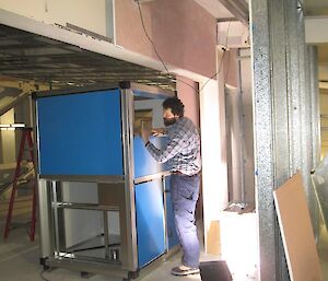 Wayne the plumber working on a section of heating and ventilation metal duct work which is painted blue.