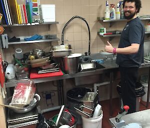 Man in kitchen washing dishes, with many piles of washing up to do