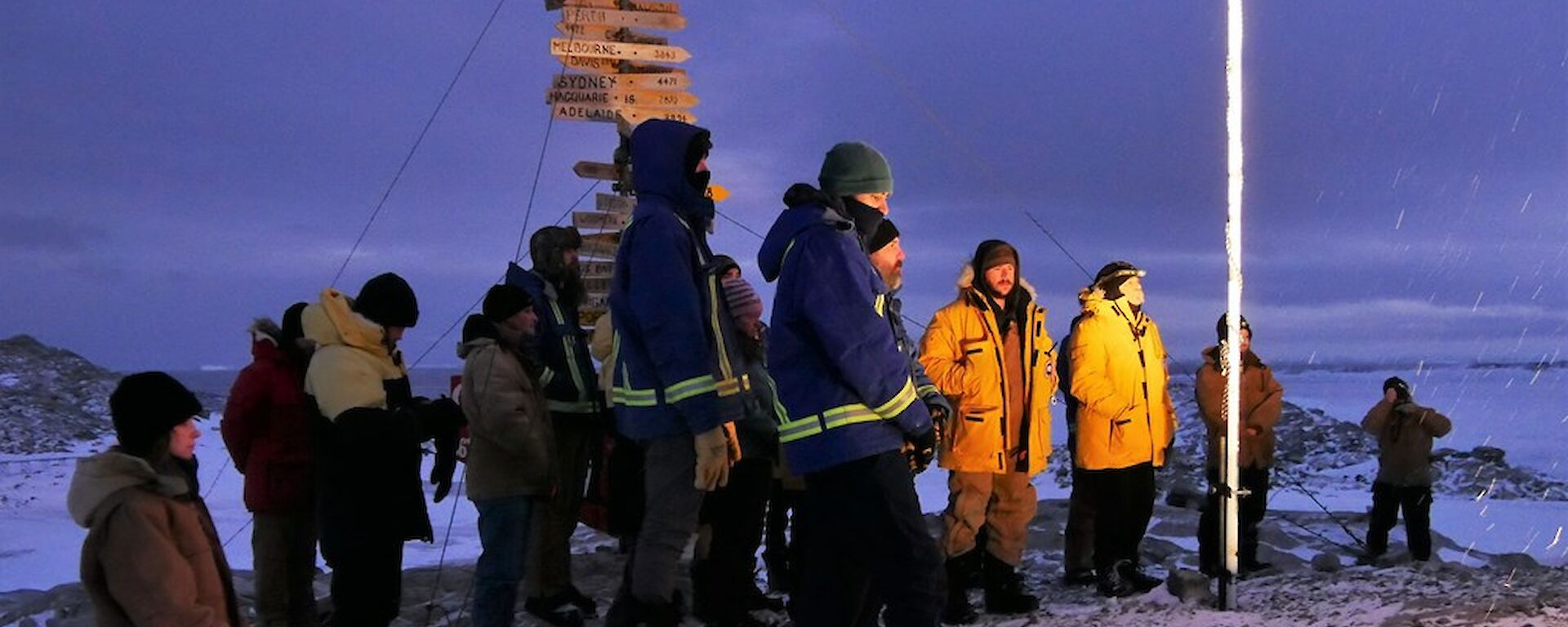 Group of expeditioners standing under the flag poles and in front of the Casey sign for the dawn service.