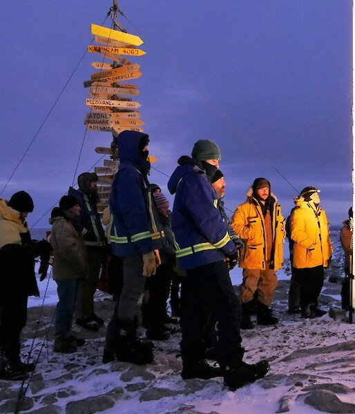Group of expeditioners standing under the flag poles and in front of the Casey sign for the dawn service.