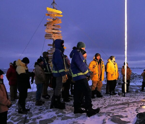 Group of expeditioners standing under the flag poles and in front of the Casey sign for the dawn service.