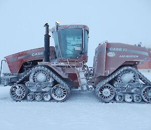 A large red Quadtrak tractor parked out in the snow covered in frost.