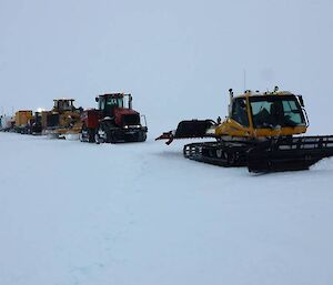 A snow groomer in front of three Quadtrak tractors all in a line hauling equipment back to Casey station.