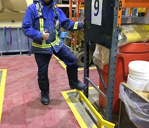 Kieran standing next to the yellow guardrail in front of pallet racking in the green store.