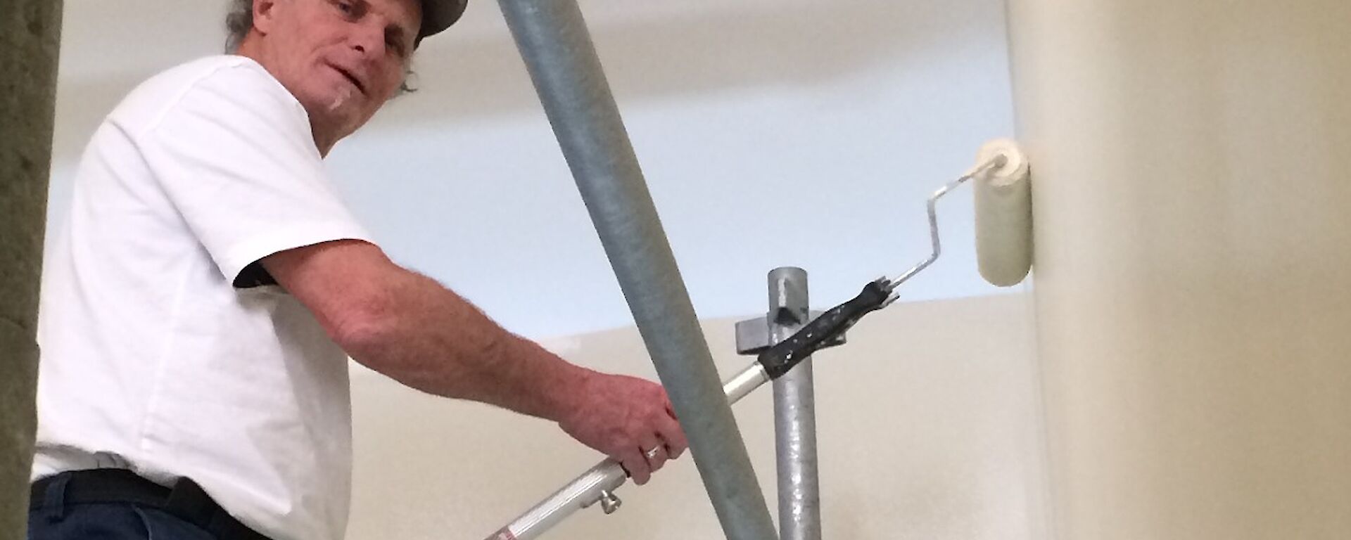 Jeff painting walls with a paint roller from scaffolding.