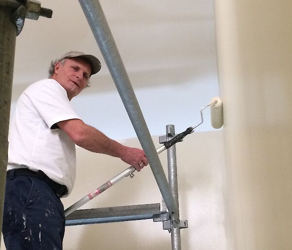 Jeff painting walls with a paint roller from scaffolding.