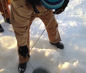 Mick looking in the hole drilled in the ice while holding on to the rope that is tied to the sampling tube in the water below the ice.