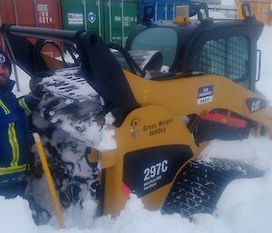 The senior mechanical supervisor digging out a skid steer machine that is almost buried in snow as well as the engine bay completely full of snow.