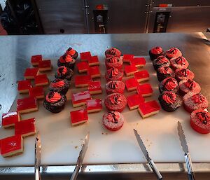 A platter of red cupcakes, chocolate cupcakes decorated with red icing and a red jelly slice.