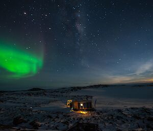 Browning’s Hut in the foreground with an Aurora and the moon in the background on a star filled night looking north.