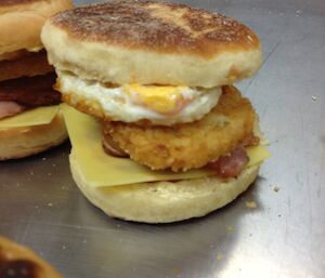 Bacon, egg, hash brown, cheese between a muffin that has been sliced in half.