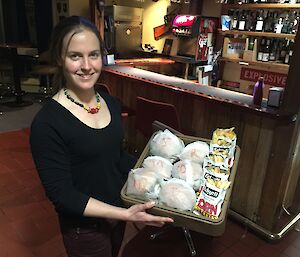 Rachel carrying a tray full of burgers and chips with the bar area in the background.
