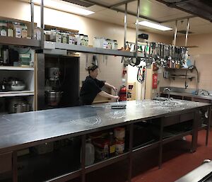 Chef cleaning the stainless steel kitchen bench with a squeegee after scrubbing it with hot soapy water.