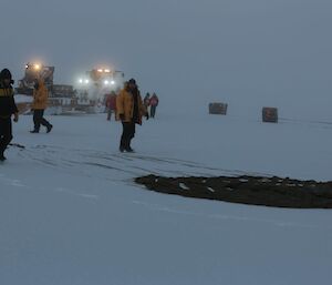 Expeditioners walking around the parachute on the ground with lights from the machinery in the background.