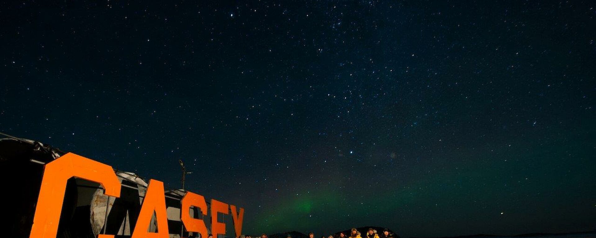 Another group photo, this time in front of the Casey sign at the wharf, as an aurora dances in the background.