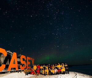 Another group photo, this time in front of the Casey sign at the wharf, as an aurora dances in the background.