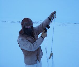 Rachel holding the tape measure that has a metal rod at the end which wedges under the sea ice, and the thickness is read from the top of the ice.