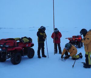 Expeditioners drilling holes in the sea ice to place marker canes with two quad bikes at the location.