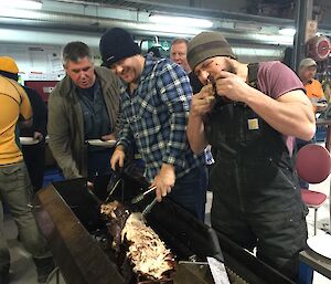 Guys carving the spit roast with one having an early taste test of the meat.