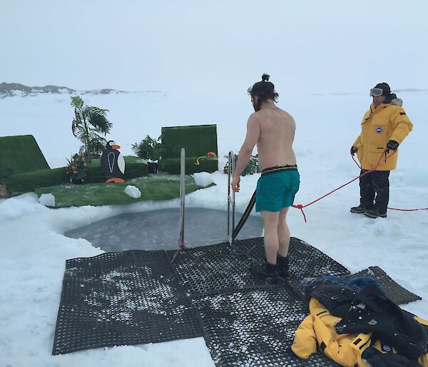 Nate with safety line attached ready to hope into the sea ice plunge pool with the fake palm trees and outdoor setting in the background.