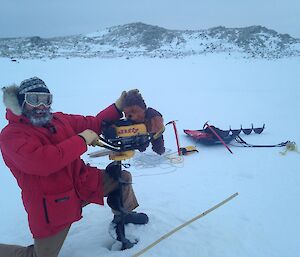 Mick & Walter (stuffed soft toy) both holding on to a Jiffy ice drill that is utilised to drill the sea ice with the water testing equipment in the background.