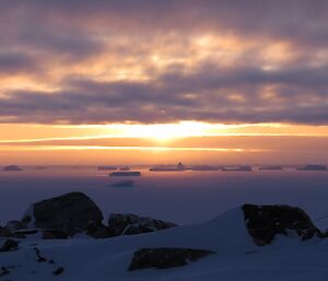 Sun rising through the cloud cover with a section of ice bergs which are stuck in the sea ice lit up in the distance.