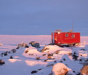 The red field hut bathed in light with the frozen ice cap in the background.
