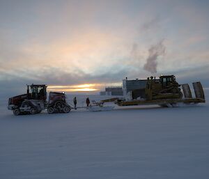 The QuadTrac tractor towing the recovery sled carrying a bulldozer with the sun rising through the clouds in the background.