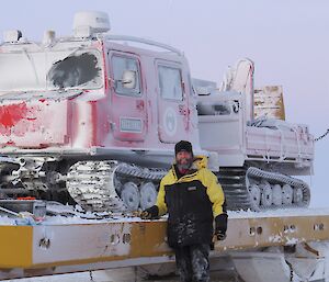 Expeditioner standing next to the snow covered red Haggland over snow vehicle which is loaded on a recovery sled.