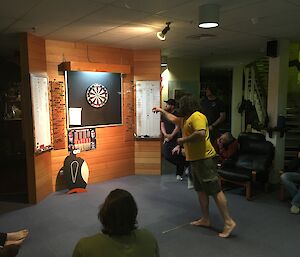 Expeditioner playing darts with Shifty (penguin cut out) watching on from under the dart board