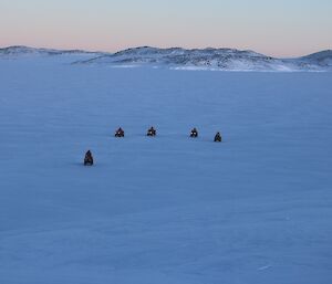 Five quad bikes some distance away returning from a ride on the sea ice coming towards the photographer with land in the background.