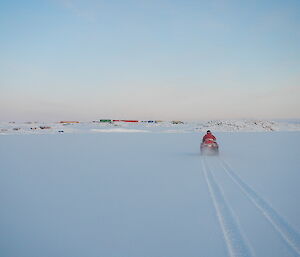 Riding a quad bike away from the camera through the fresh new snow with the station of in the distance.