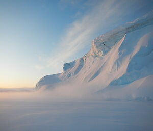 A wave shaped ice cliff with a blue sky backdrop.