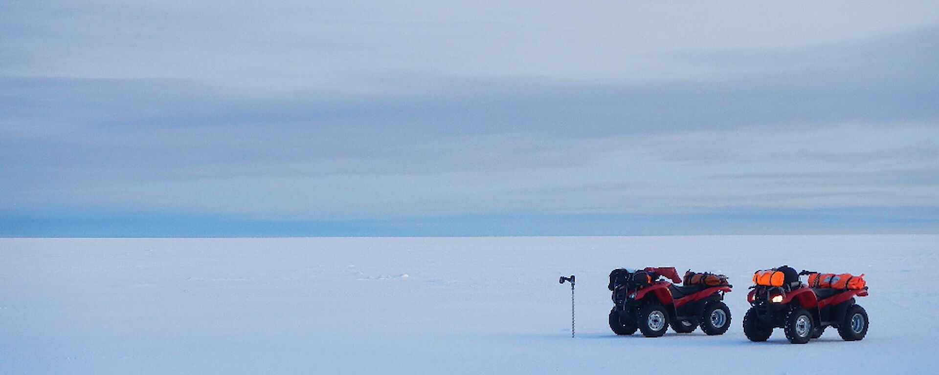 Two quad bikes and an ice drill standing up on the sea ice with nothing else as far as the eye can see.