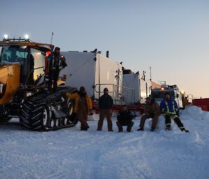 Four expeditioners lined up next to the Case tractor towing two traverse vans.