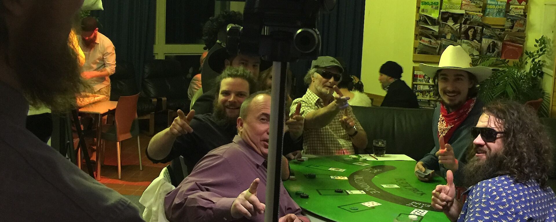 Group of people sitting at the black jack table while being filmed with the video camera on tripod in the foreground.