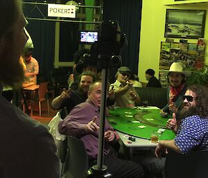 Group of people sitting at the black jack table while being filmed with the video camera on tripod in the foreground.