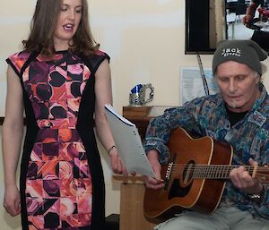 Jeff playing the guitar sitting on a stool with Rachel standing next to him as they sing a duet.