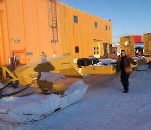 Expeditioner standing beside a large yellow sled used for transporting heavy machinery.