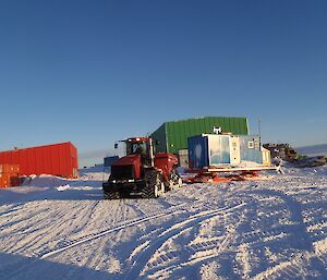 Red QuadTrac tractor towing a blue generator van on a sled.