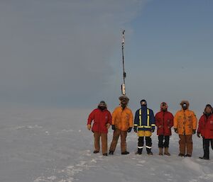 Six expeditioner standing in front of the Automatic weather station.
