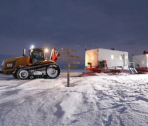 The tractor with two sled vans parked in front of a direction sign.