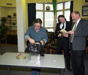 Expeditioner taking the first items out of the old biscuit tin that was used as the time capsule as another reads a letter that was in the tin.