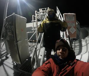 Two expeditioners at the base of the stairs of the fuel farm during a fuel transfer.