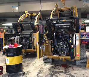 Looking at the back of two skid steer machines parked side by side with rear engine bay doors open.