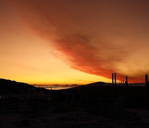 Bright orange/red sunset with the dark silhouette of hills and science building in the foreground.