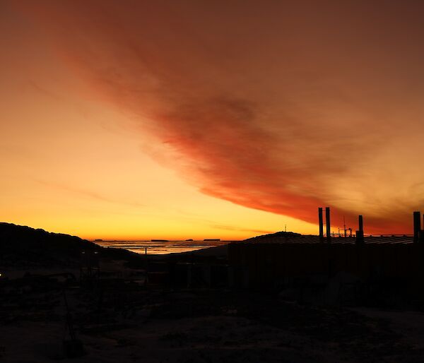 Bright orange/red sunset with the dark silhouette of hills and science building in the foreground.