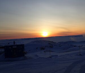 The sun just above the horizon as it moves behind the low cloud cover.