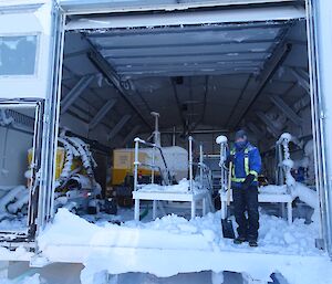 Expeditioner with a shovel standing in the large doorway as he digs out the snow from inside the workshop building.